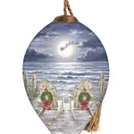Hand-painted glass ornament featuring two chairs with wreaths on a moonlit beach, with Santa's sleigh flying across the night sky.