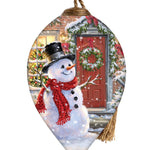Hand-painted glass ornament featuring a snowman with a top hat and red scarf standing in front of a festive holiday door with a wreath.