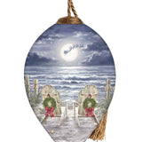 Hand-painted glass ornament featuring two chairs with wreaths on a moonlit beach, with Santa's sleigh flying across the night sky.